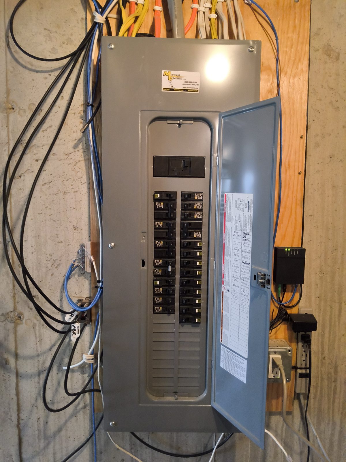 Residential electrical panel with the door open, mounted on a plywood wall, evaluated during a home inspection