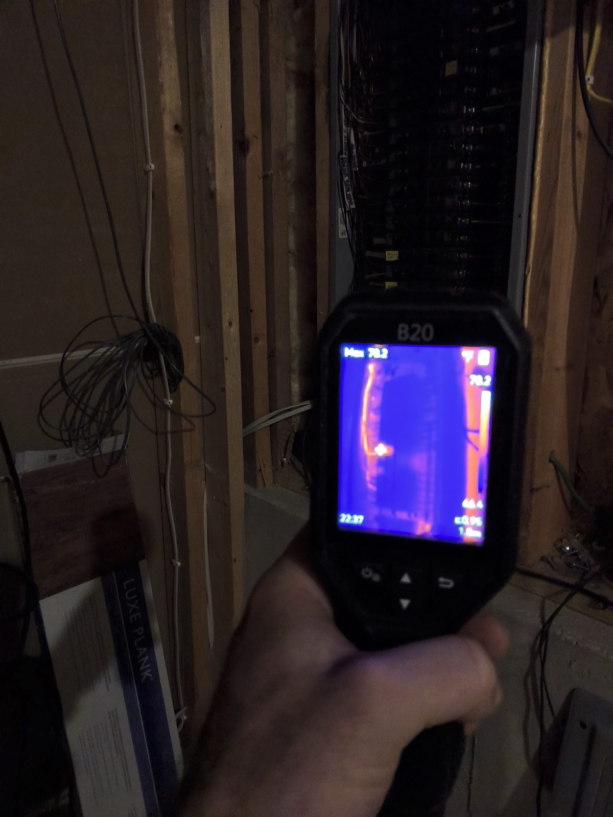 Inspector holding a thermal camera up to an open stud wall to find hidden temperature and moisture differences